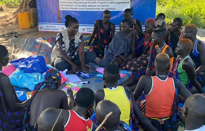 Women and girls seated in a circle on the floor listening to someone speaking.